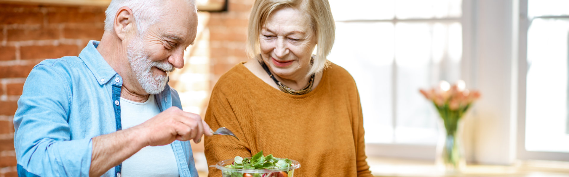 Cheerful senior couple eating salad standing together.